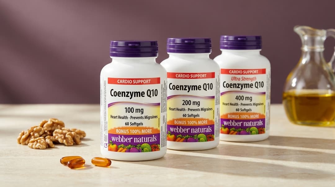Tri fľaštičky Webber Naturals Koenzým Q10 s tmavofialovými uzávermi na svetlom kamennom pulte – vpredu balenie so 100 mg, za ním 200 mg a 400 mg. Vedľa nich vlašské orechy, dve jantárové kapsuly a karafa s olejom.